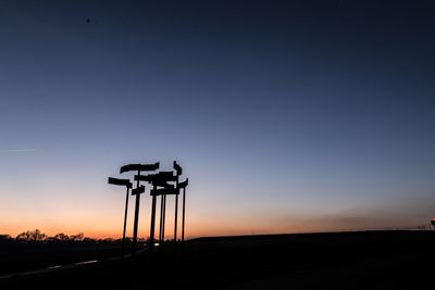 Silhouette cranes against clear sky at sunset