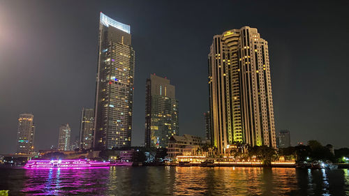 Illuminated modern buildings in city against sky at night