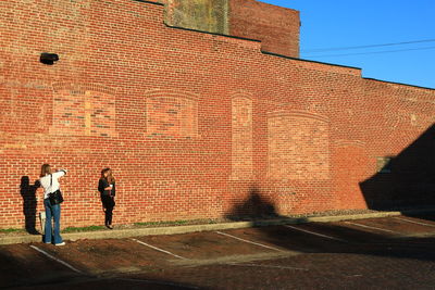 Wide angle of two girls taking pictures against brick wall