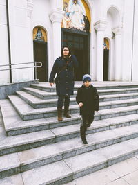 Full length of mother with son moving down on steps against church