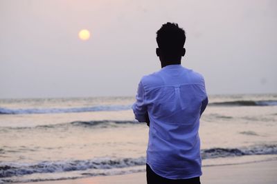 Rear view of woman standing at beach during sunset