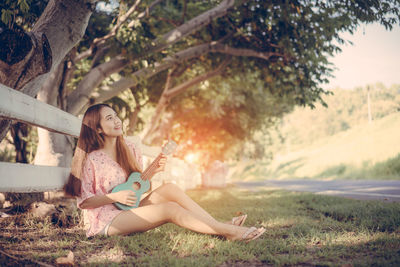 Full length of woman playing ukulele while sitting on grass 