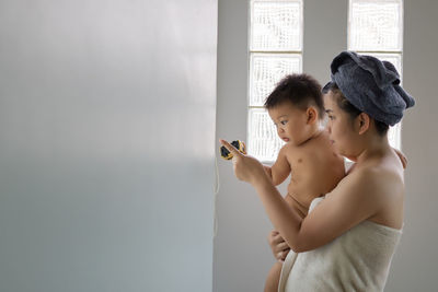 Side view of mother holding naked son in bathroom