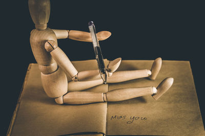 Wooden figurine holding pen while sitting on open book against black background