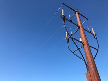 Low angle view of telephone pole against clear blue sky