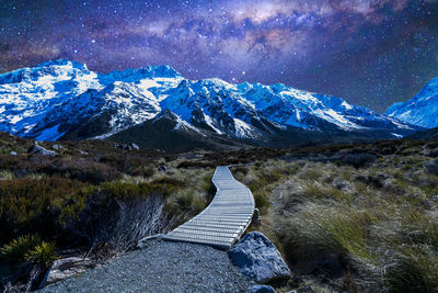 Boardwalk leading towards snowcapped mountain against sky at night