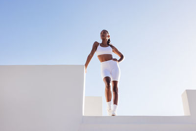 Full length of woman exercising against clear blue sky