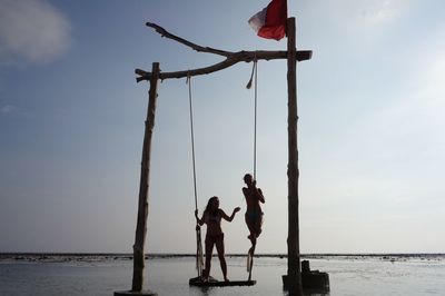 Women standing on swing over sea against sky