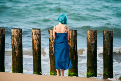Young blue-haired woman in long dark blue dress with cute tattoo on her shoulder blade on beach