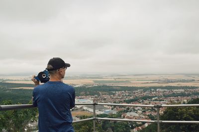 Rear view of man standing at observation point with cityscape in background against sky