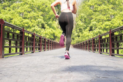 Low section of woman jogging on footbridge in park