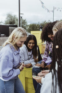 Female friends smiling while using mobile phone outdoors