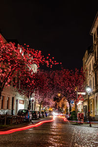 Illuminated street amidst buildings against sky at night