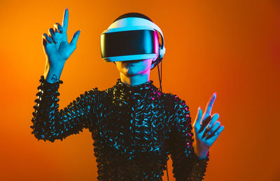 Young woman with shaved head wearing virtual reality glasses against orange background