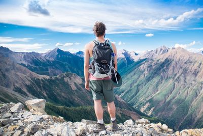 Man standing on rock looking at mountains against sky