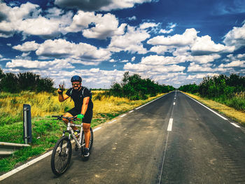 Man riding bicycle on road against sky