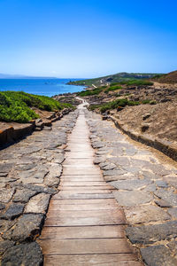 Footpath leading towards sea against clear blue sky