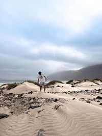 Rear view of woman walking on sand at beach against sky