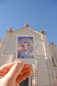 Cropped hand holding photograph against church