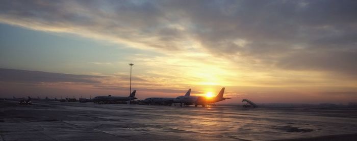 Airplane on runway against sky during sunset