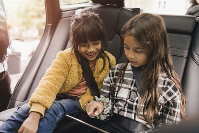 Sisters using digital tablet while sitting in electric car