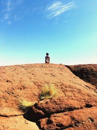 Man standing on rock in desert against clear blue sky