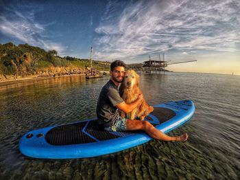 Portrait of man embracing dog on surfboard in sea