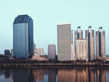 Modern buildings by river against clear sky