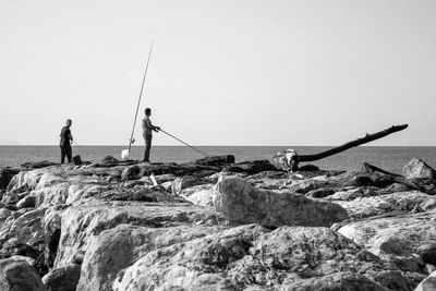 Fishing rod on rock by sea against clear sky