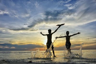 Silhouette people standing on beach against sky during sunset