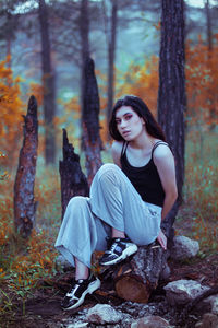 Portrait of woman sitting on rock in forest during autumn