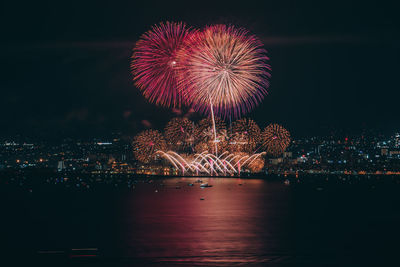 Firework display over illuminated city against sky at night