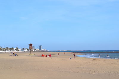 People on beach against clear blue sky