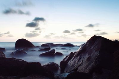 Rocks on beach against sky during sunset