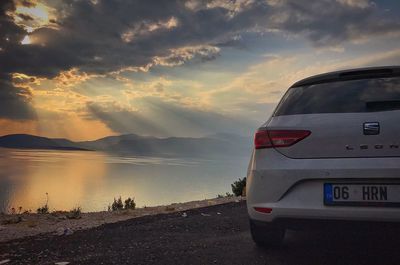 Car on road by lake against sky during sunset