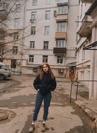 Full length portrait of young woman standing against building in city