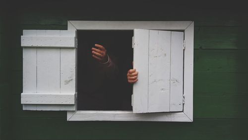 Human hands on white wooden window shutters