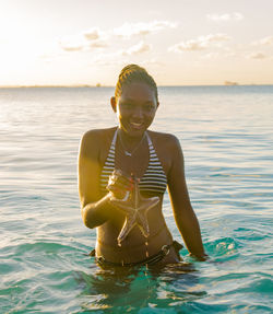 Portrait of smiling woman standing in sea against sky