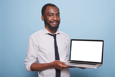 Portrait of man using laptop while standing against blue background