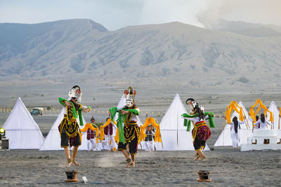 People wearing traditional clothing while dancing at desert against mountains