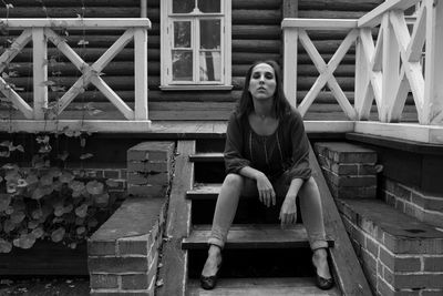 Portrait of young woman sitting on steps against log cabin