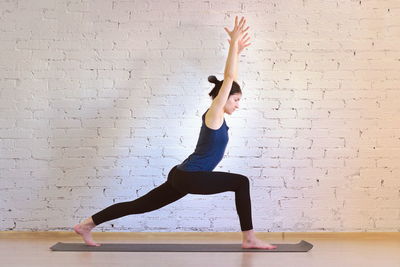 Full length of woman with arms raised against wall
