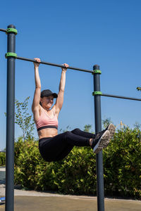 Happy woman in sportclothes working out on the sports ground in sunny summer day, training her abs