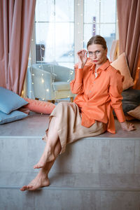 Woman in the studio sits on background of window in glasses and bright clothes