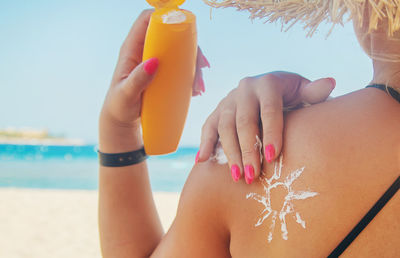 Midsection of woman holding bottle at beach against sky