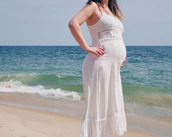 Midsection of pregnant woman standing at beach against clear sky