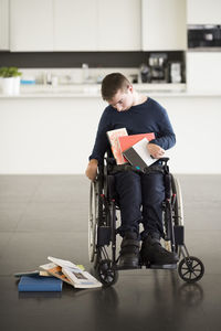 Man with cerebral palsy looking at fallen books while sitting on wheelchair at home
