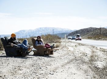 People sitting on road by mountain against sky