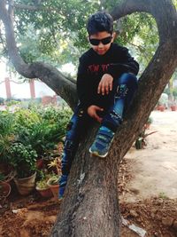 Full length of man wearing sunglasses on tree trunk