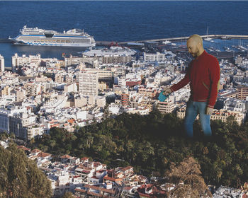 Rear view of man standing by sea against buildings in city
